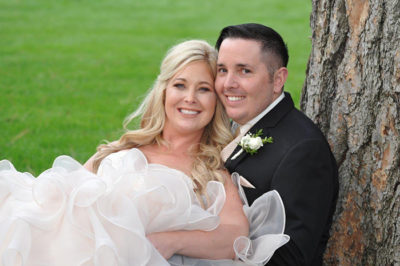 Bride and groom sitting together against a tree